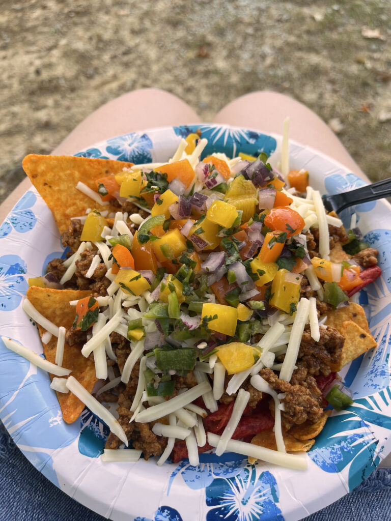 A paper plate filled with a bed of doritos and toppings of taco meat, pico, and shredded cheese.